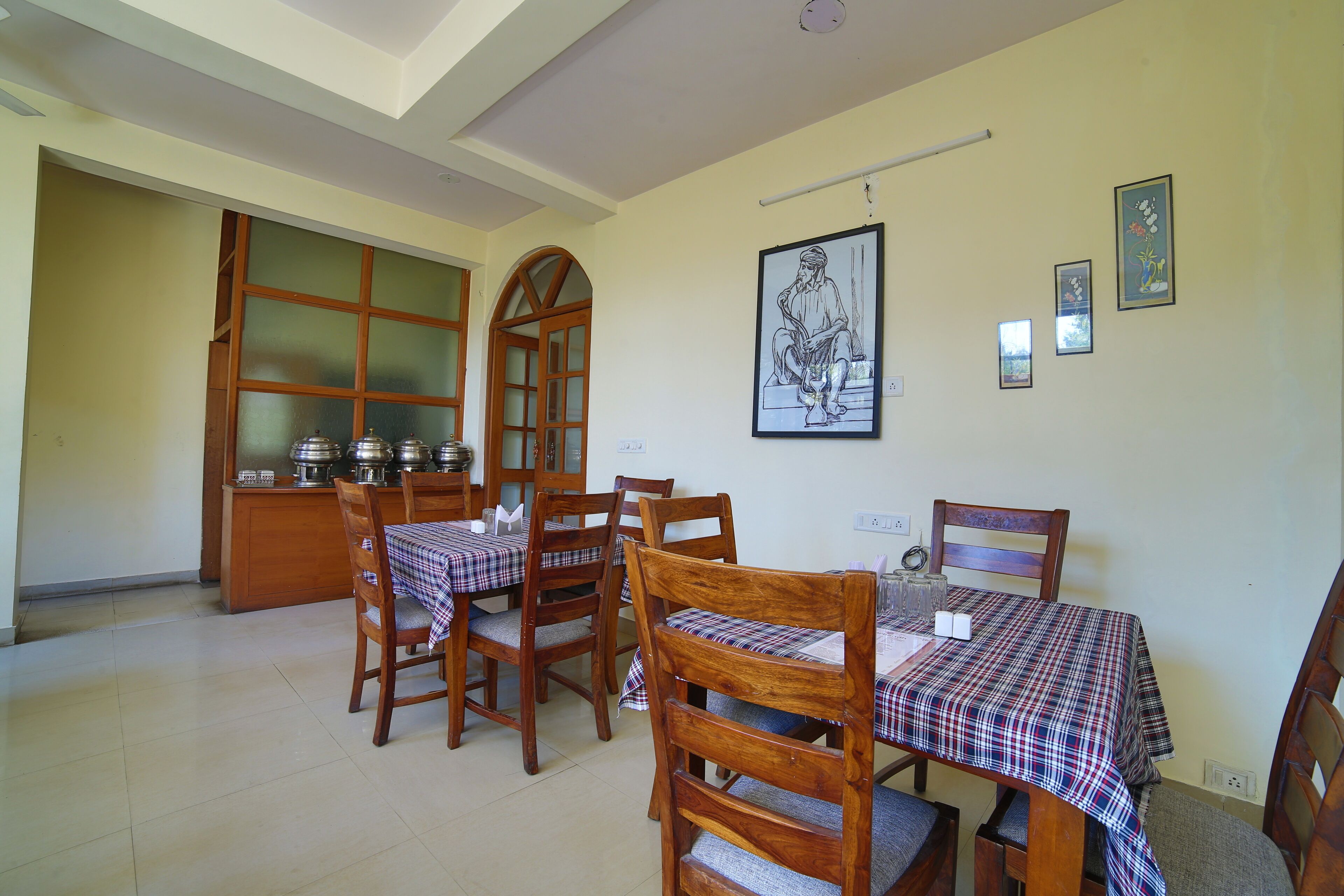 A dining area with wooden chairs and tables, a kitchen area with cabinets, and artwork on the walls.