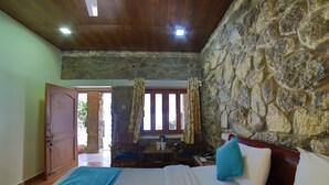 Ein Schlafzimmer mit Steinwand, Holzboden, einem Bett mit blau-weißer Bettwäsche, einem Holztisch mit Stühlen und einem Fenster mit Vorhängen.