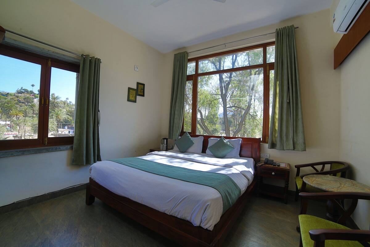 Ein Schlafzimmer mit einem Bett, einem Nachttisch, einem Sessel und einem Fenster mit Vorhängen.