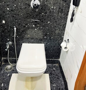 Un baño con inodoro blanco, cabezal de ducha de mano y teléfono fijo en la pared.