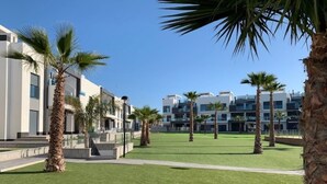 A modern building complex with multiple residential units, a well-maintained lawn, and palm trees. - Superb terrace apartment with pool view-Oasis Paradise (Guardamar del Segura)