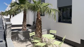 A modern building with white walls and blue windows. There are palm trees and green chairs in the courtyard. - Superb terrace apartment with pool view-Oasis Paradise (Guardamar del Segura)
