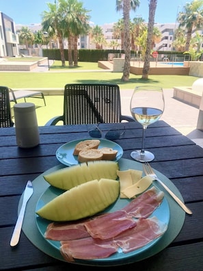 A table with a plate of food, a glass of white wine, and a speaker.