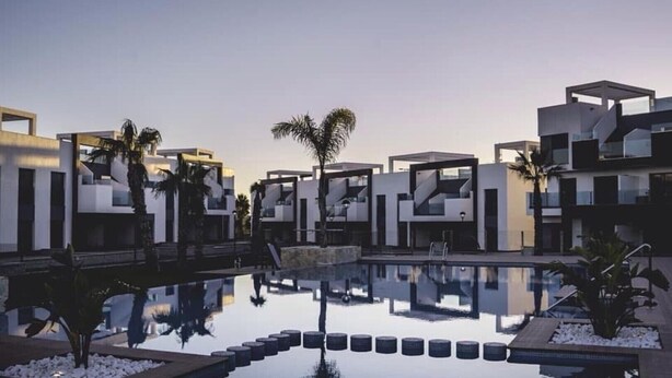 A modern hotel with a reflective pool, palm trees, and contemporary architecture. - Superb terrace apartment with pool view-Oasis Paradise (Guardamar del Segura)