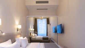 A hotel room with a bed, bedside lamps, a TV, and a door leading to a bathroom. - Tiflis Opera Aparthotel (Tbilisi)