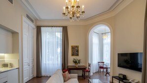 A spacious living room with a sofa, a glass coffee table, a TV, and a dining area with a table and chairs. - Tiflis Opera Aparthotel (Tbilisi)