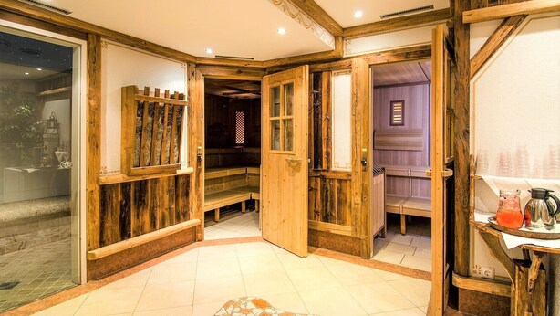 Un intérieur en bois, avec un sol carrelé, un banc en bois et une table sur laquelle se trouvent une bouilloire et un verre.