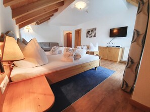 A bedroom with a wooden bed, a desk, a lamp, a TV, and a wardrobe. - Hotel Daniel (Ischgl)