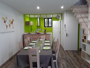 Uma sala de jantar com uma mesa posta para quatro pessoas, uma cozinha com paredes verdes e uma escada.