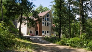 Ein zweistöckiges Haus mit geneigtem Dach, umgeben von dichtem Wald.