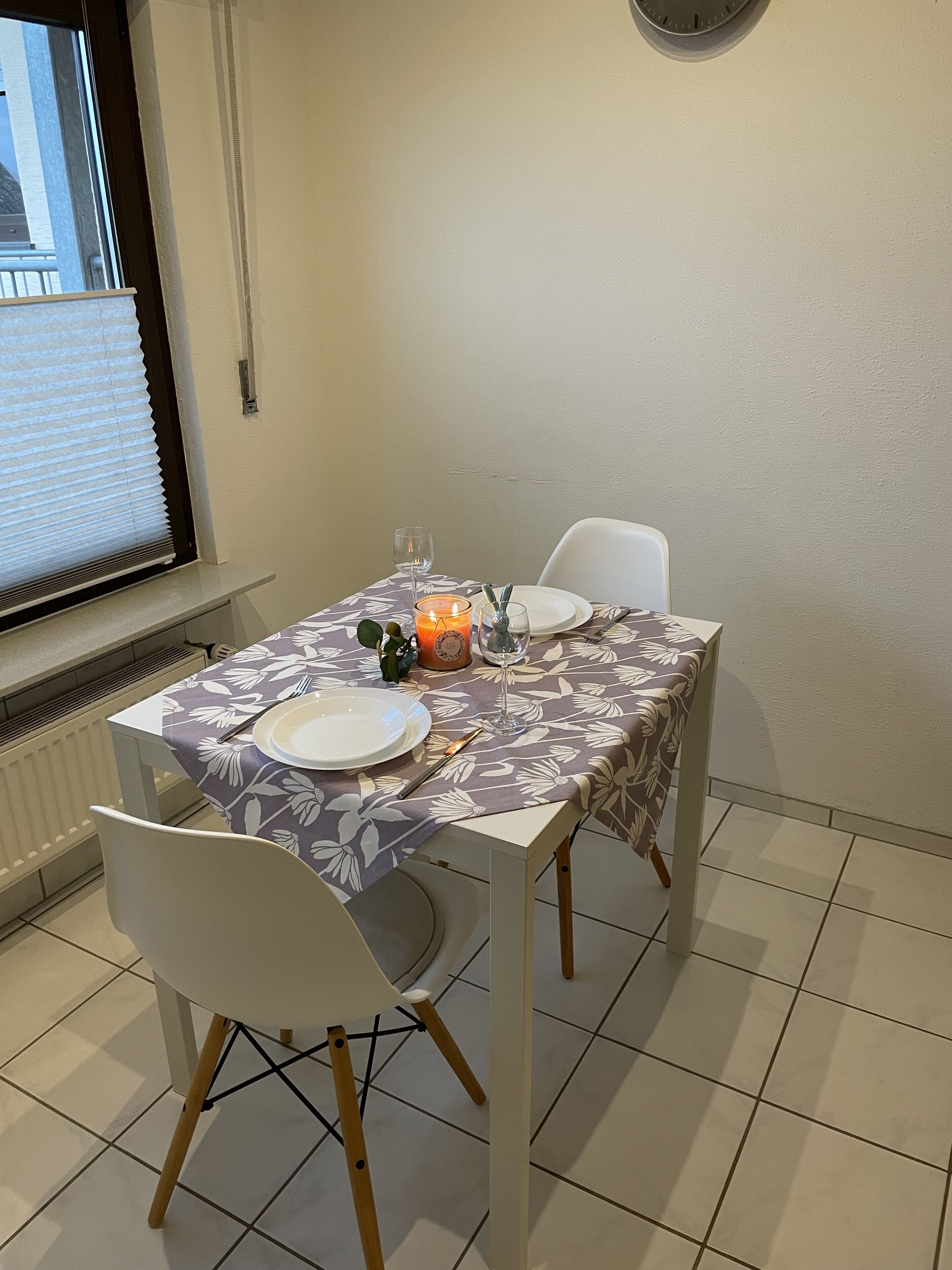 Una mesa de comedor dispuesta con platos, cubiertos, una vela y un vaso de agua.