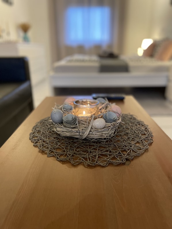 A candle in a glass holder on a wooden table with a woven placemat, surrounded by decorative eggs.