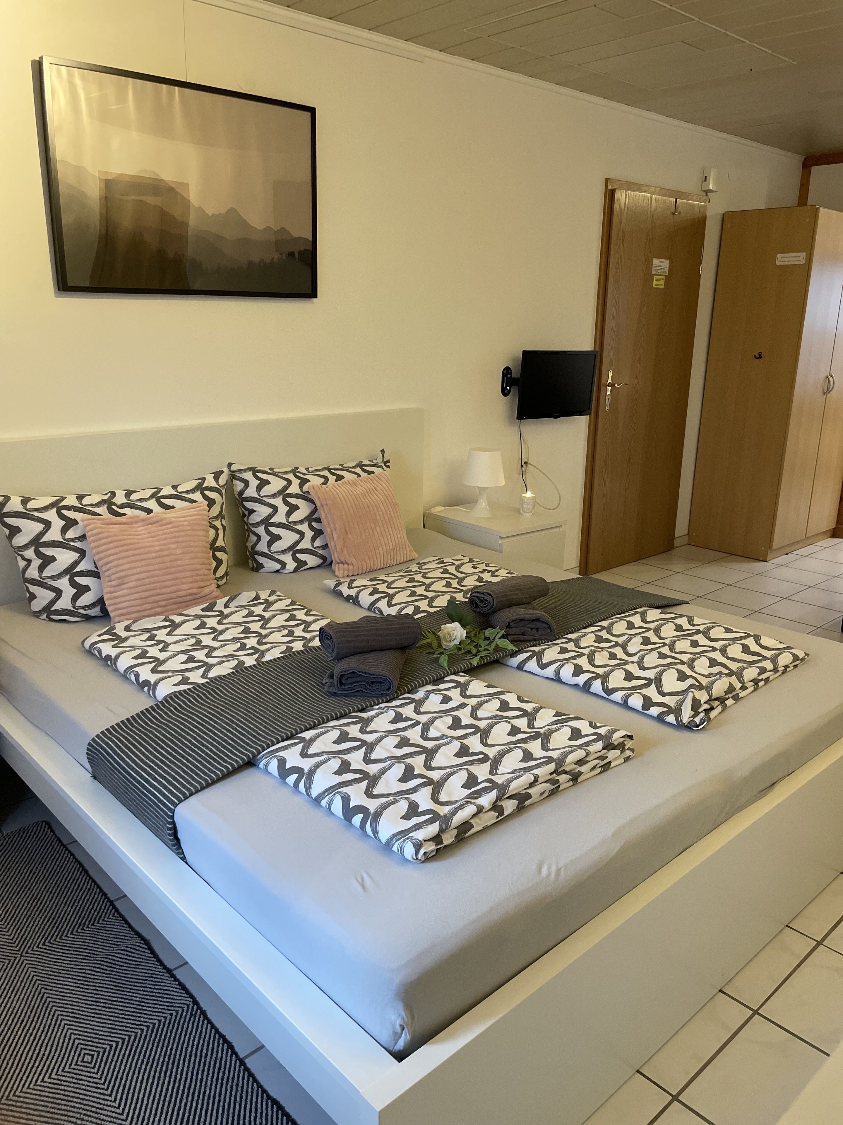 Een opgemaakt bed met gestreepte kussens en een nachtkastje met een lamp en een kleine plant.