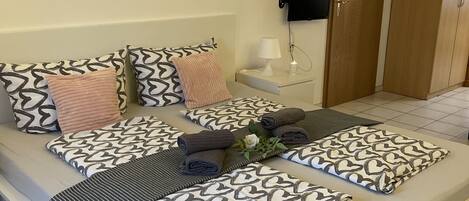 Una cama ordenada con almohadones estampados y una mesita de noche con lámpara y una pequeña planta.