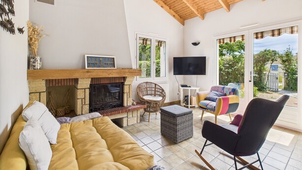 Ein Wohnzimmer mit Kamin, Sofa, Fernseher und Blick ins Freie.