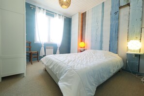 A bedroom with a large bed, a chair, a desk, and a window with curtains.