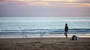 Ein Strand mit zwei Angelruten und einer Person, die spazieren geht.