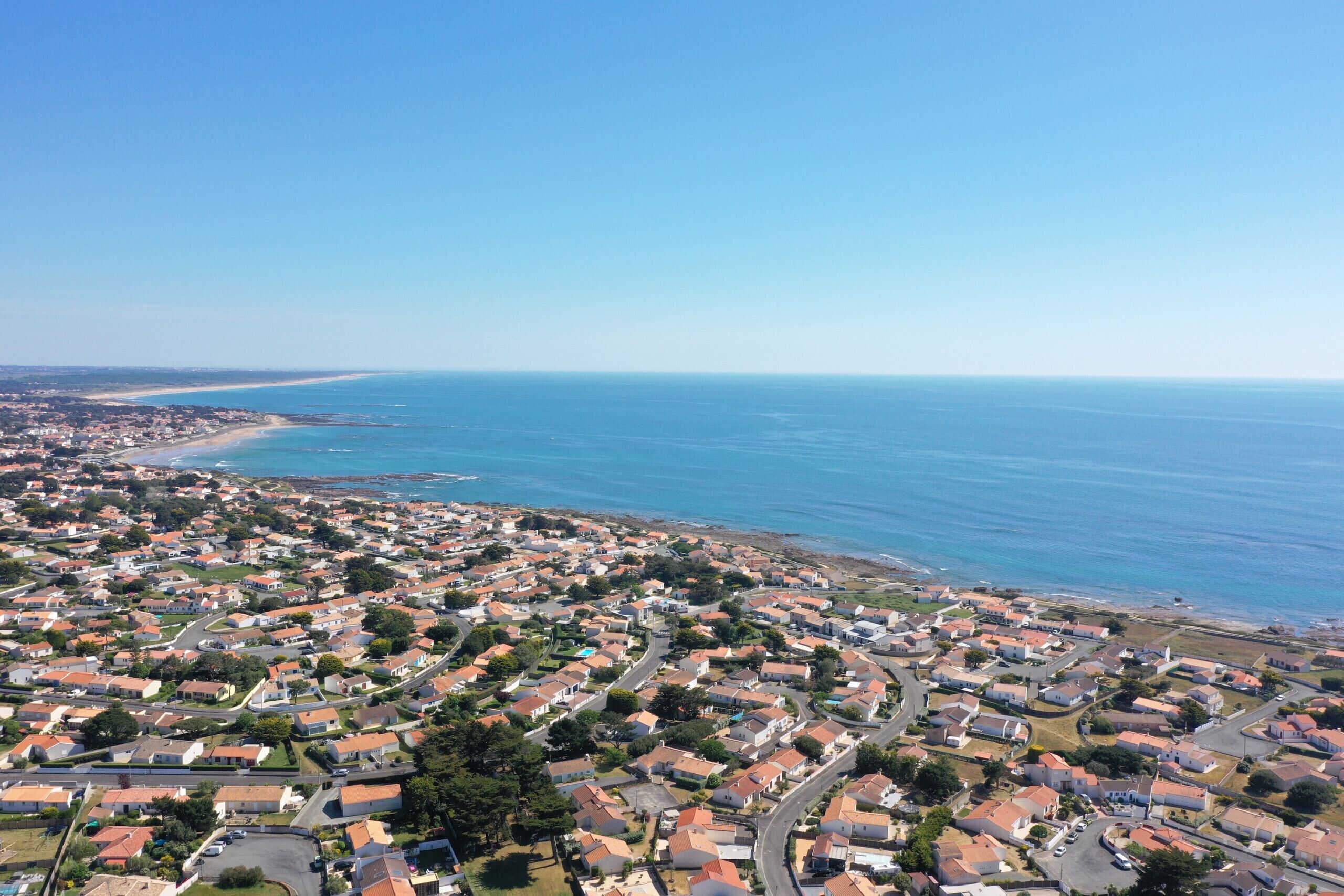 An aerial view of a coastal residential area with houses, roads, and a beach.