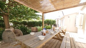 Eine Holzterrasse mit Picknicktisch, umgeben von Grünpflanzen und einem Grill.