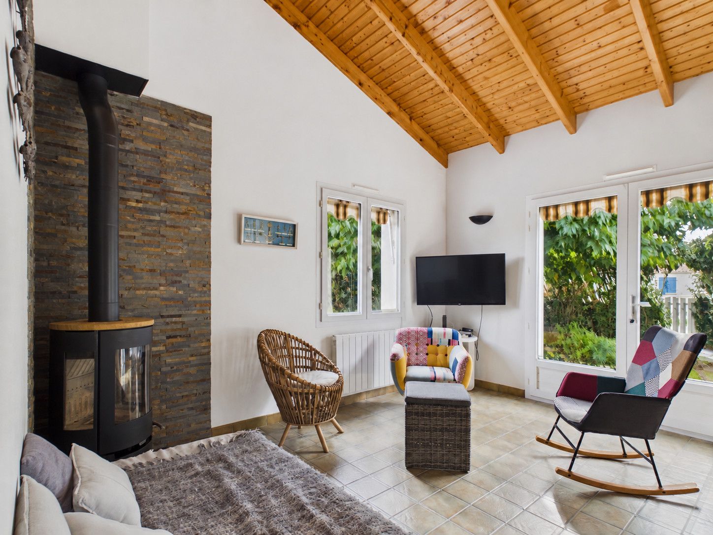 A living room with a fireplace, wicker furniture, a television, and large windows.