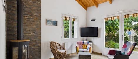Una sala de estar con chimenea, muebles de mimbre, televisor y ventanas amplias.
