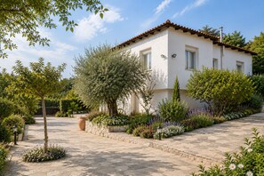 A two-story building with a tiled roof, surrounded by a garden with various plants and flowers.