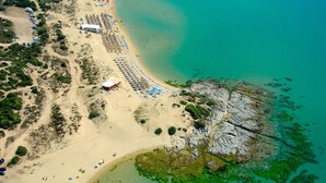 An aerial view of a beach with rows of umbrellas and a rocky outcrop in the water.