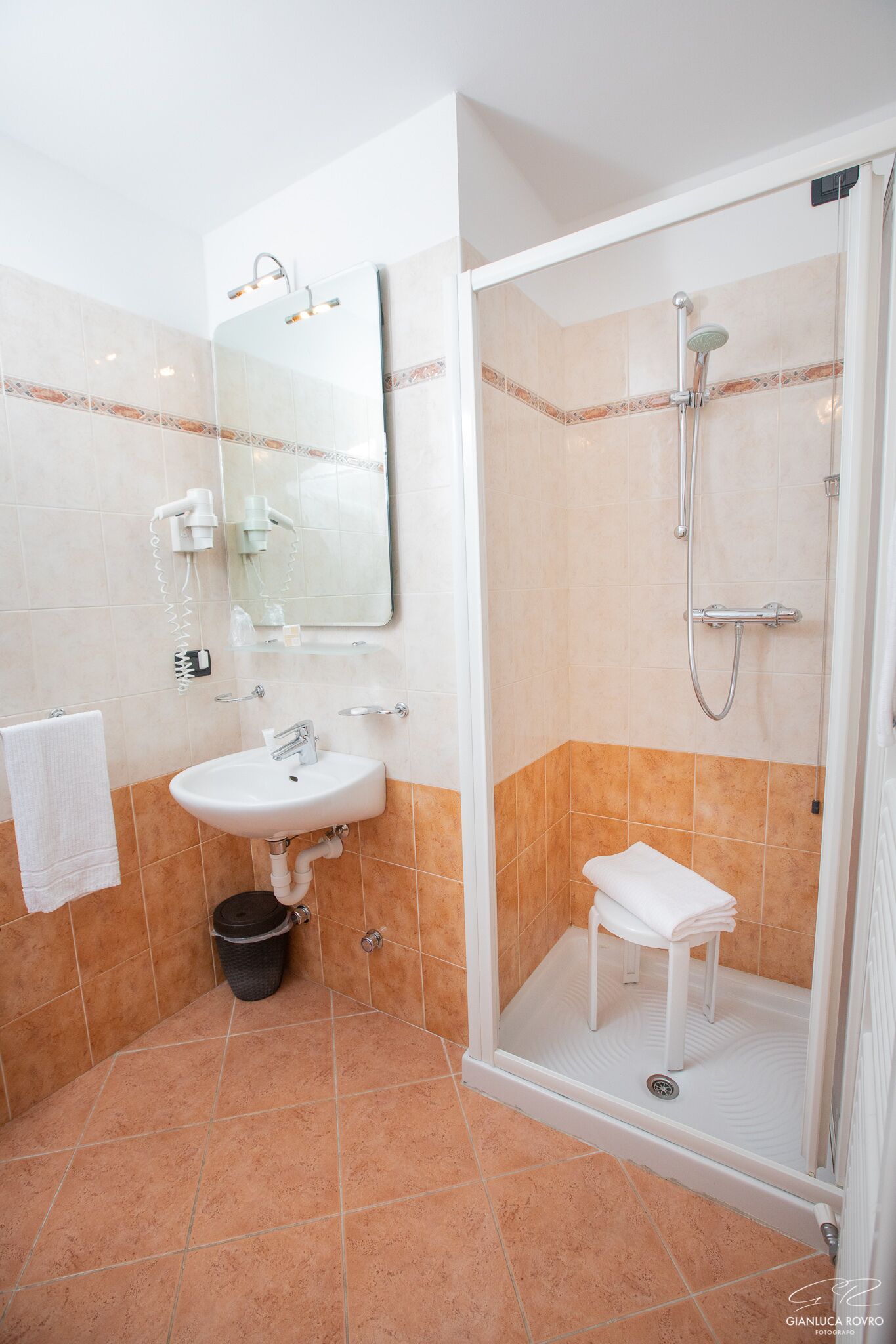Een badkamer met een wastafel, spiegel, douche en een klein krukje.