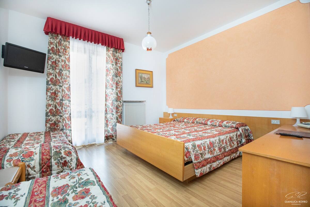 A bedroom with a bed, a desk, a chair, a television, and a window with curtains.
