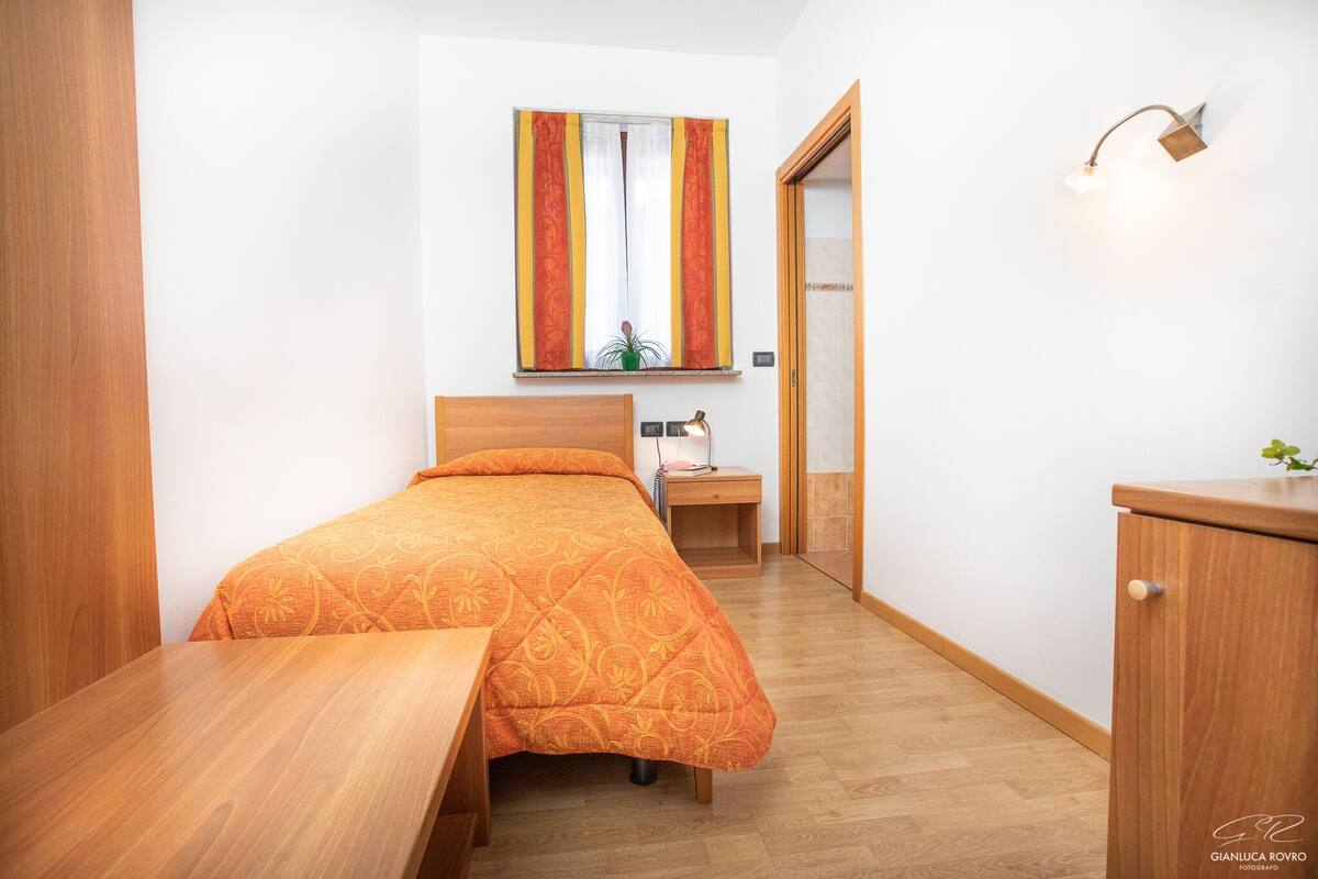 A compact bedroom with a wooden bed, bedside table, and a small desk.