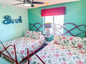 A bedroom with two beds, a ceiling fan, a window with blinds, and a wall-mounted lamp. - Beach Club I 3E (North Myrtle Beach)