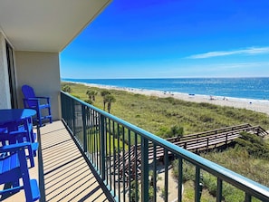 A balcony with a view of the beach, outdoor furniture, and a wooden staircase leading to the beach.
