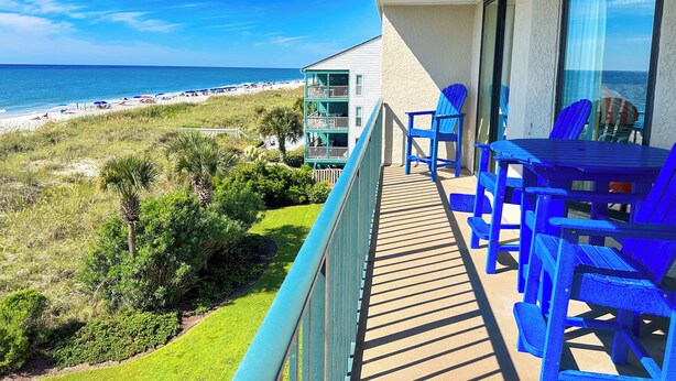Un balcon avec vue sur la plage, une table et des chaises bleues.