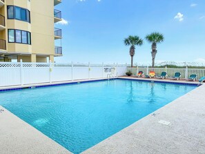 A swimming pool with a white fence, palm trees, and a building with balconies.