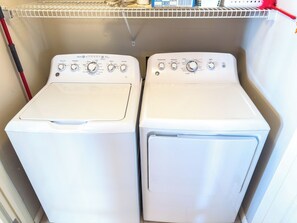 Two front-loading washing machines in a laundry room with a metal shelf above. - Beach Club I 3E (North Myrtle Beach)
