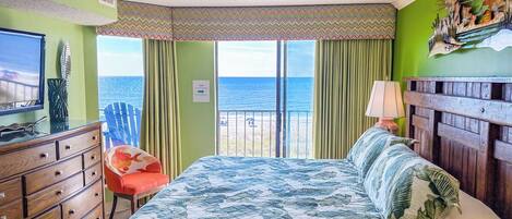 A bedroom with a bed, a dresser, a chair, a lamp, and a view of the sea.