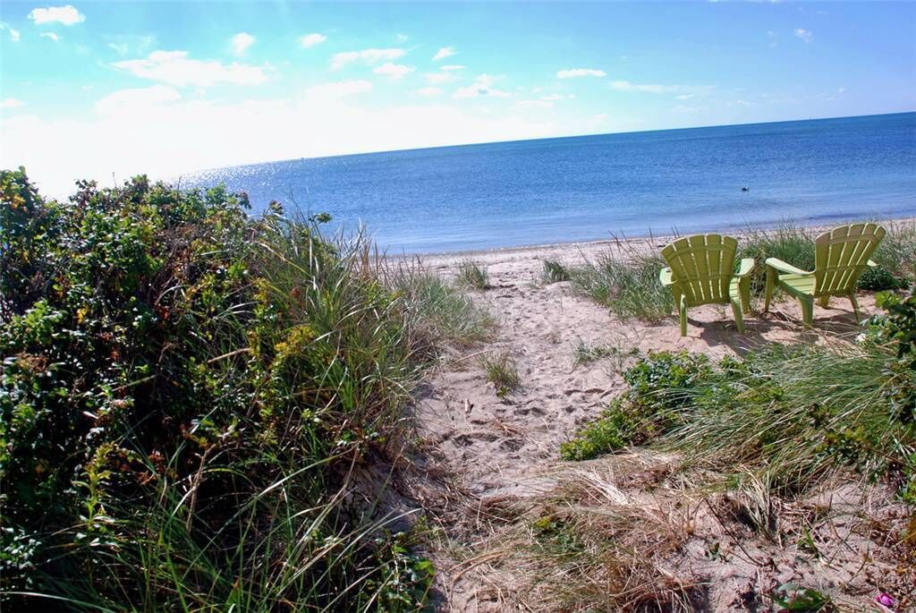 A sandy beach path leading to two green Adirondack chairs facing the ocean.
