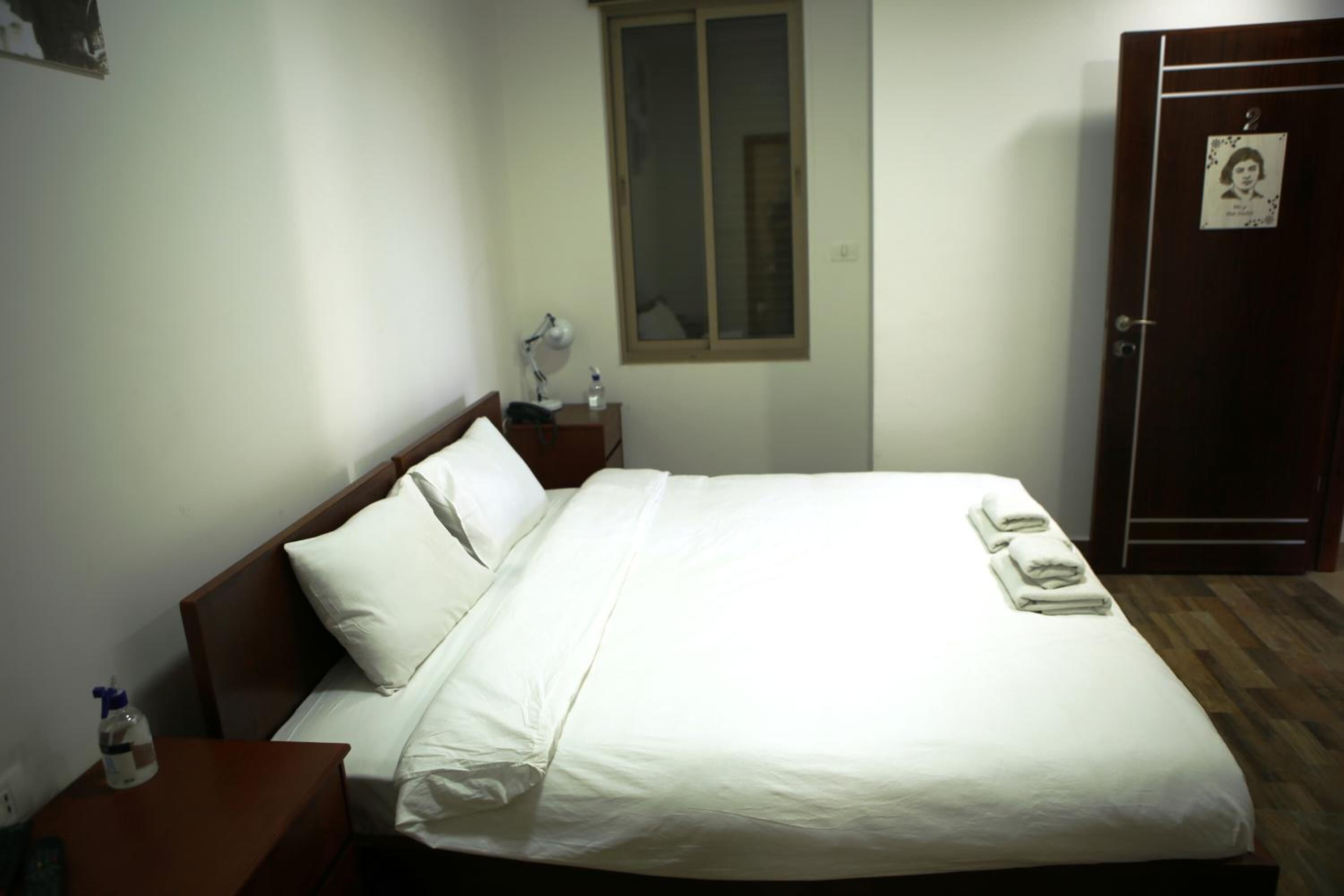 A neatly made bed with white linens, a bedside lamp, and a small table with a bottle.