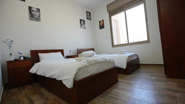 Un dormitorio limpio y bien iluminado con una cama de madera, una mesita de noche, una lámpara y un ventanal con persianas.