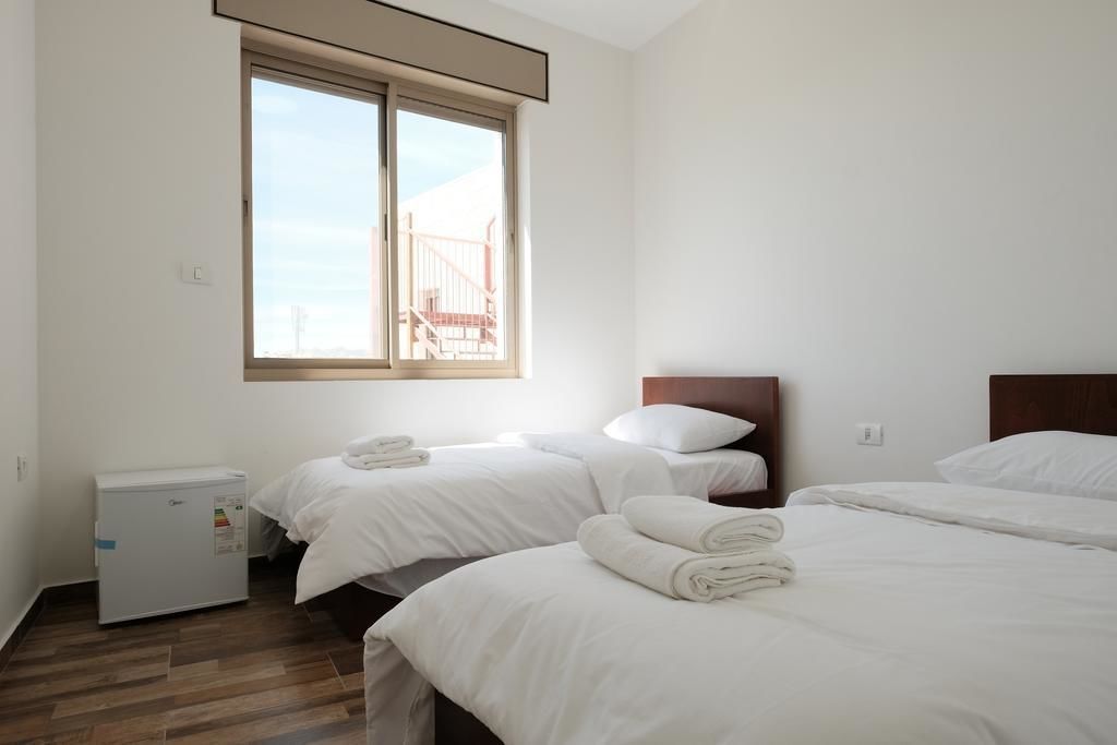 Habitación de hotel con dos camas, un refrigerador pequeño y ventana con vista a un edificio.