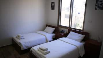 Een hotelkamer met twee eenpersoonsbedden, een houten hoofdbord, een nachtkastje met telefoon en fles, en een raam met uitzicht op de stad.