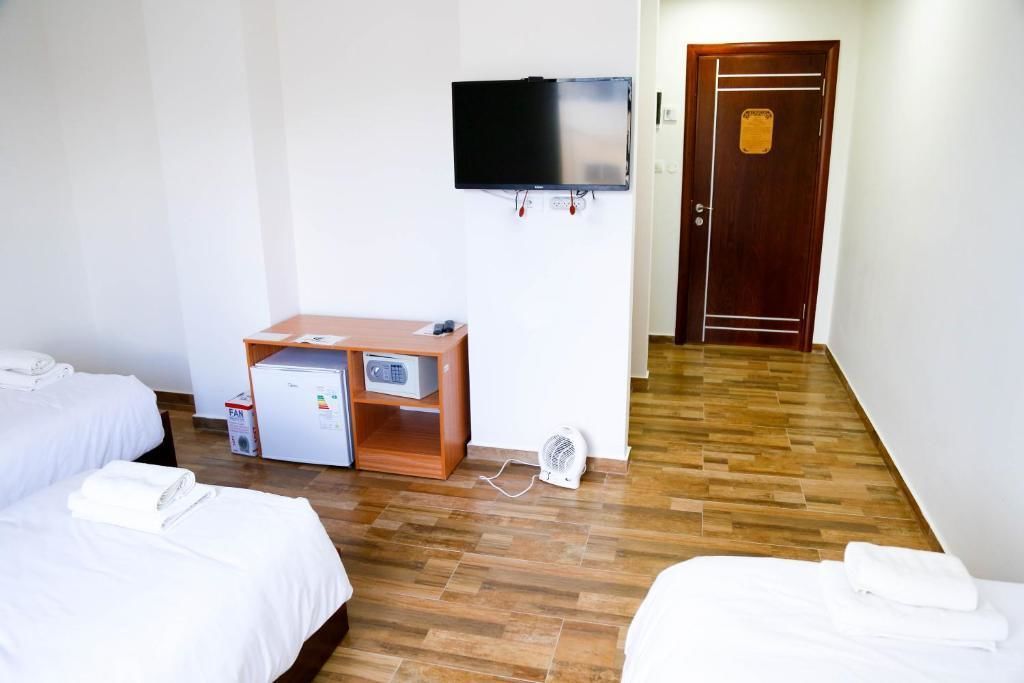 A hotel room with two beds, a TV mounted on the wall, a desk with a computer and a fan, and a wooden door.