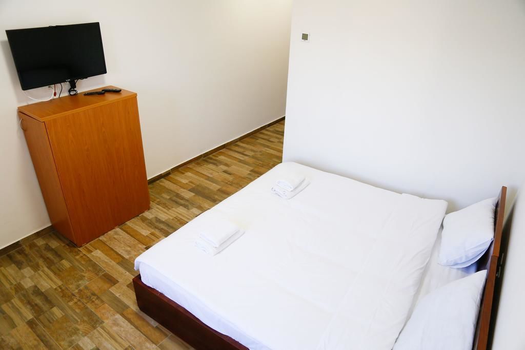 A single bed with white linens, a wooden nightstand with a TV, and a wooden floor.