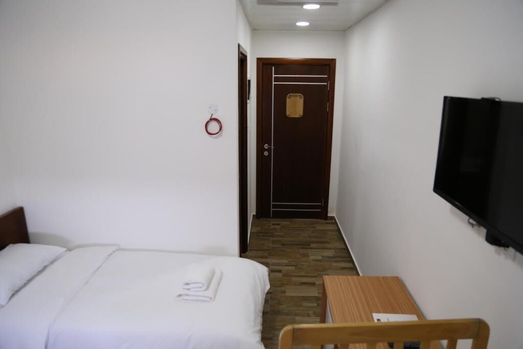 Una camera d'albergo con un letto, un tavolo di legno, una sedia, una televisione e una porta con una targa.