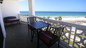 Ein Balkon mit Tisch und Stühlen, der Blick auf einen Strand mit Sonnenschirmen und Palmen freigibt.