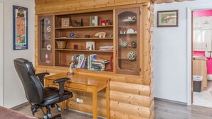 Una camera accogliente in stile baita, con una scrivania in legno, una sedia da ufficio nera e una libreria a incasso piena di libri e oggetti decorativi.