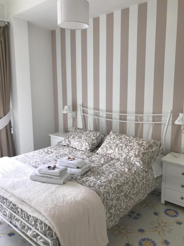 Un lit bien fait, avec une literie à motifs, une table de chevet avec une lampe et un mur à rayures.