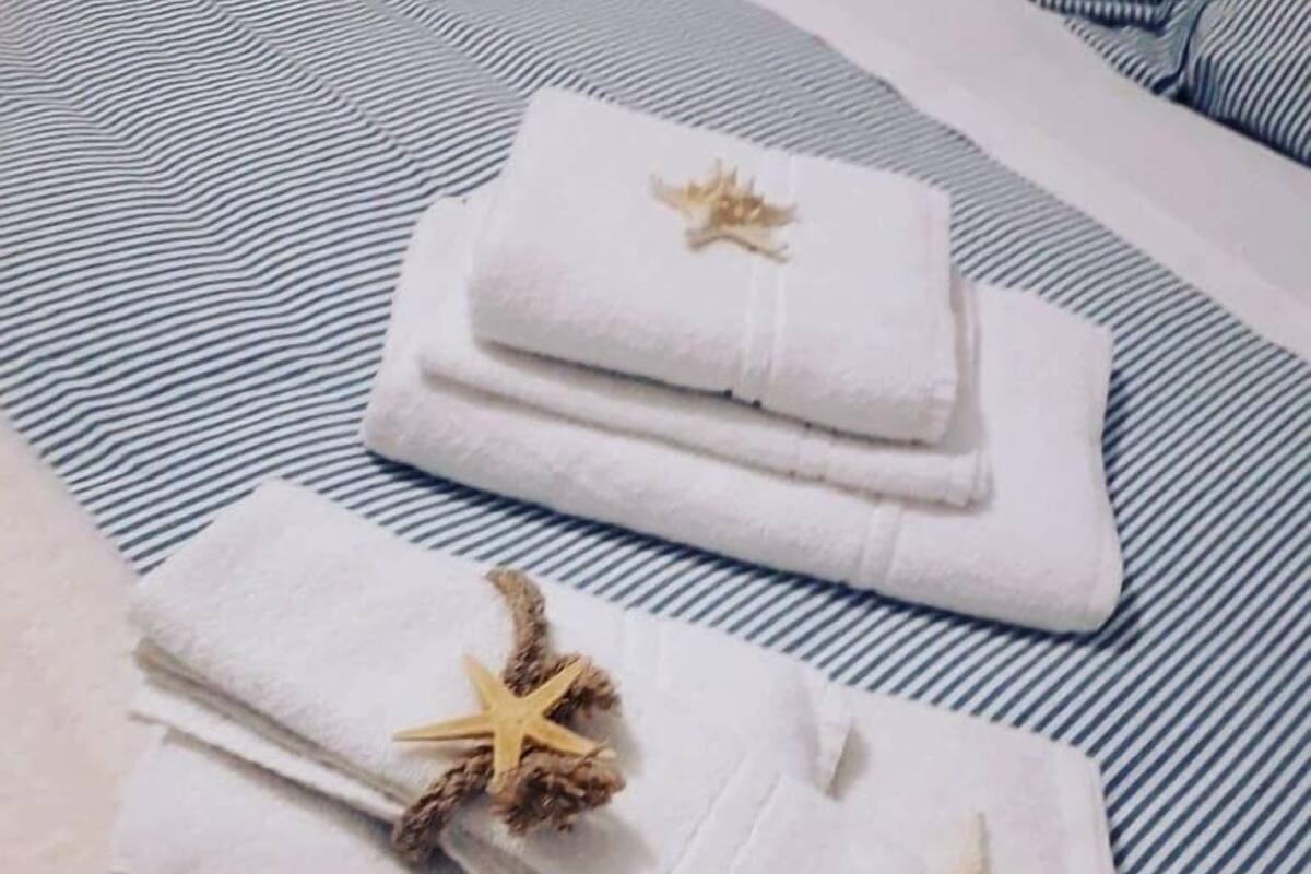 Une serviette blanche, soigneusement pliée, ornée d’une étoile de mer, posée sur un couvre-lit à rayures.