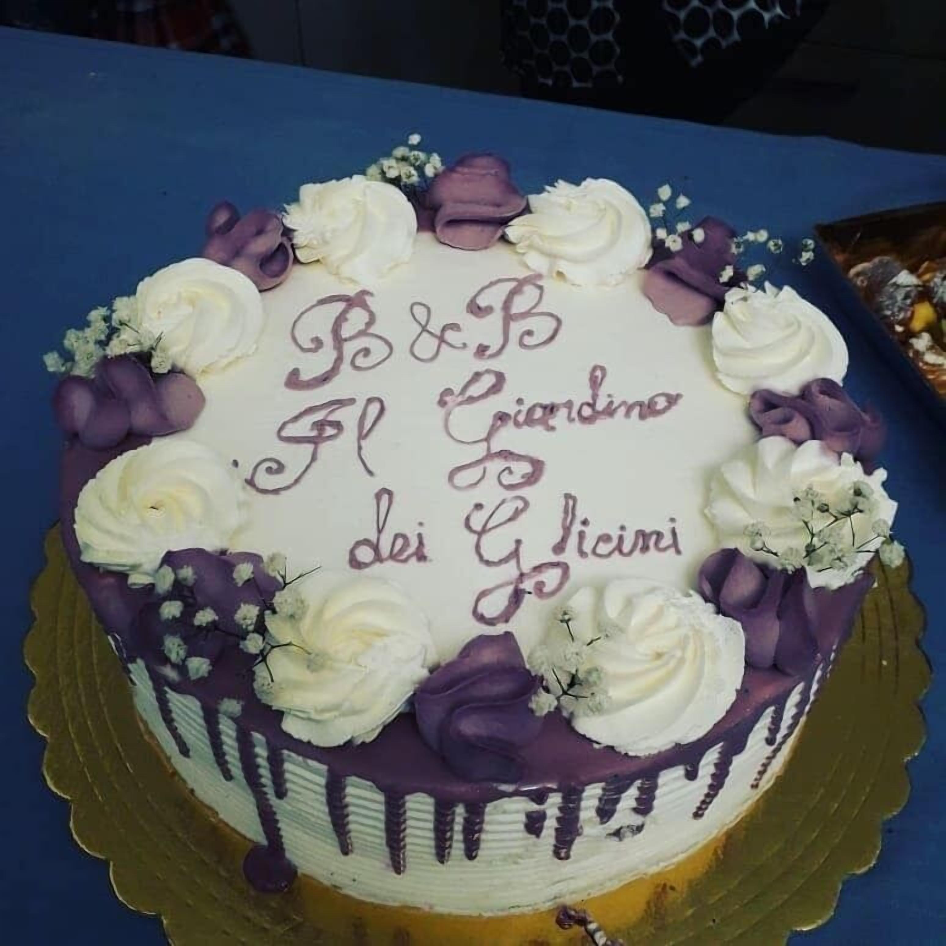 Ein Kuchen mit der Aufschrift "B&B El Giardino dei Glicini", umgeben von violetten und weißen Verzierungen.
