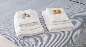 Two neatly folded white towels with seashells on a striped fabric surface.